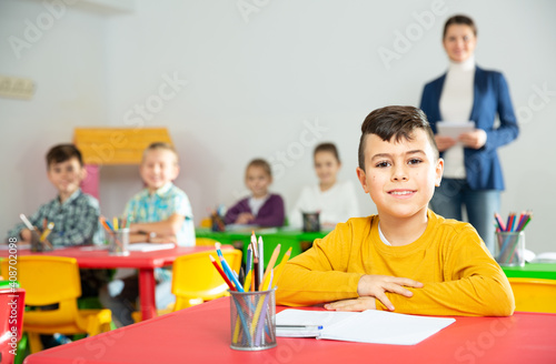 Portrait of little assiduous boy with pen and notebook at lesson in elementary school. High quality photo