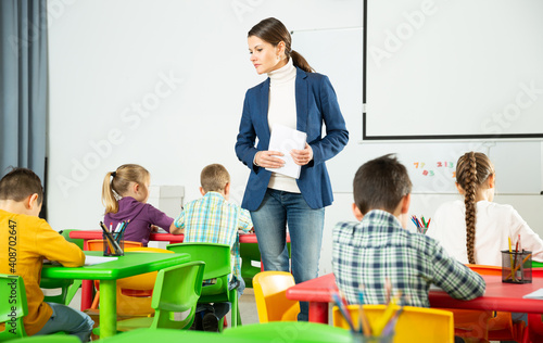 Modern young female teacher controlling learning process at lesson in primary school