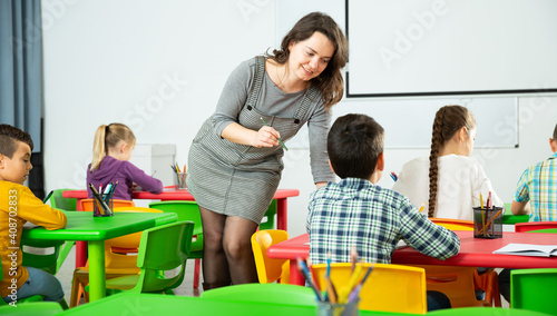 Positive boys and girls studying and female teacher helping in classroom. High quality photo