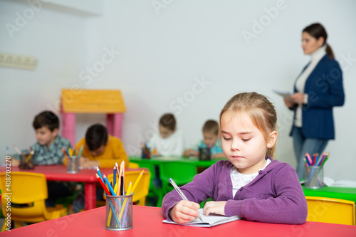 Portrait of cute diligent schoolgirl writing exercises at lessons in primary school