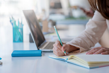 Female student study online and taking notes on their laptop at home.