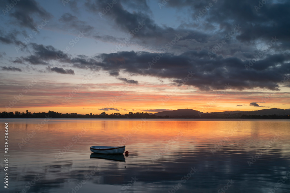 Small dinghy in bay with reflected orange golden hour light in Tauranga New Zealand.