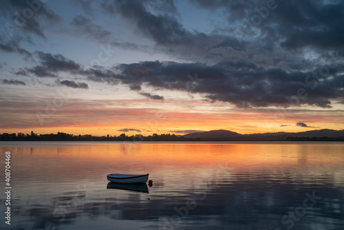 Small dinghy in bay with reflected orange golden hour light in Tauranga New Zealand. © Brian Scantlebury