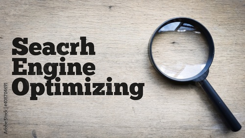 Selective focus top view text SEARCH ENGINE OPTIMIZING on wooden background with magnifying glass. SEO concept.