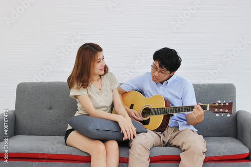 Happy young Asian couple playing acoustic guitar in living room. Sweet, Relax, Romantic and Love