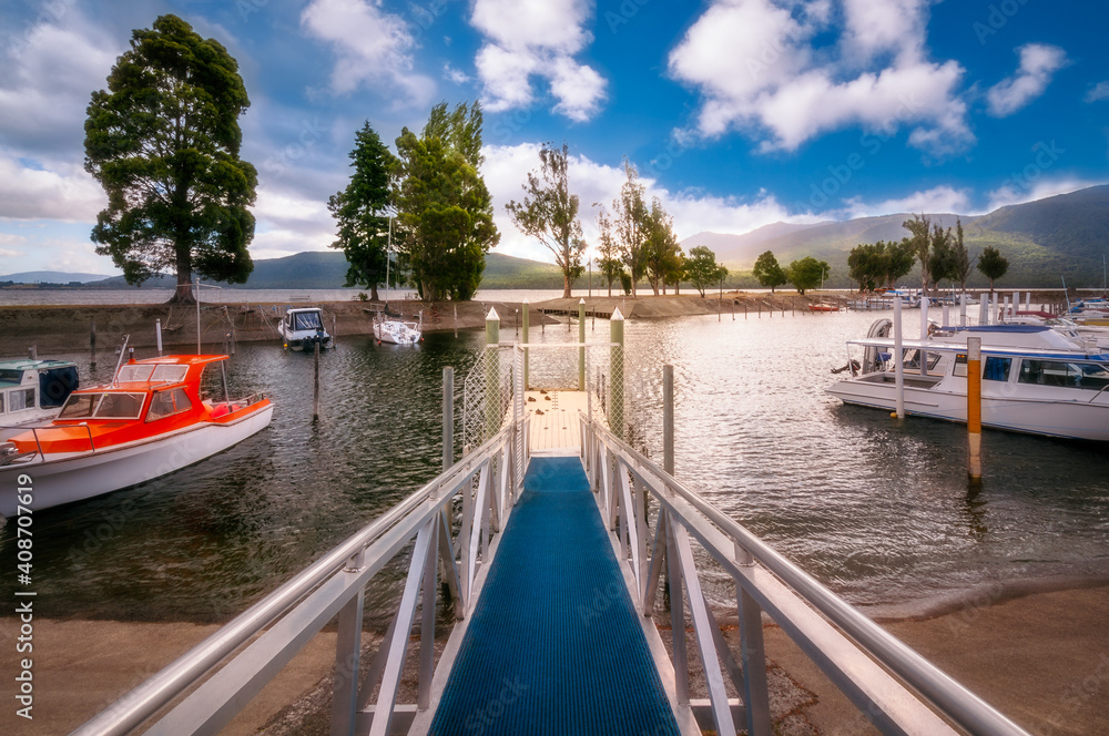 Jetty perspective and scenic view with backlit trees in the background at Te Anau Boating Club Marina, on the shore of Lake Te Anau, New Zealand, South Island, on a beautiful afternoon at golden hour.