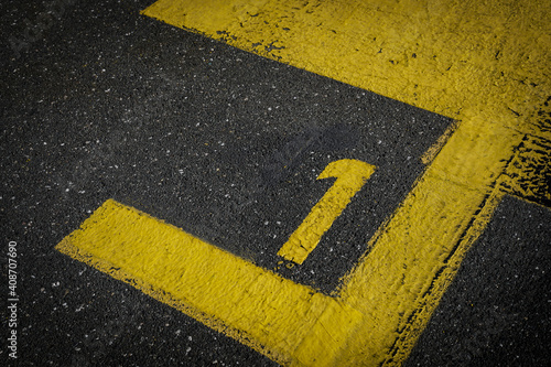 Grey asphalt road, yellow painted number one on grey street, yellow lines like a corner on the road, space for text   © YK