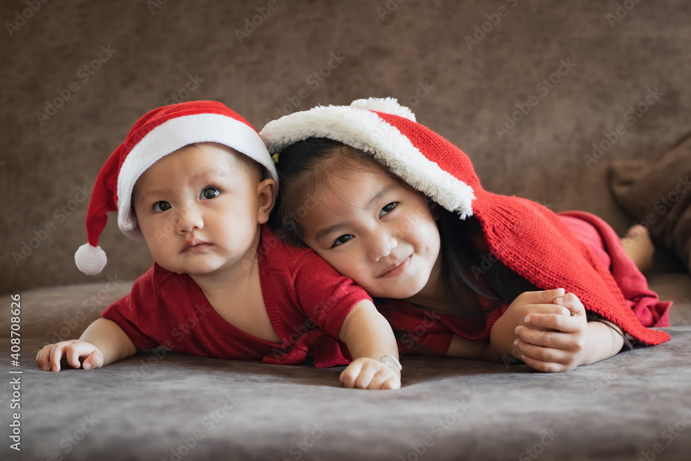 Cute asian child girl and her baby younger sister wearing christmas costume lying and relaxing on sofa bed. Happy family with children at home. Lovely siblings. Cute asian child girl and her baby younger sister wearing christmas costume lying and relaxing on sofa bed. Happy family with children at home. Lovely siblings.