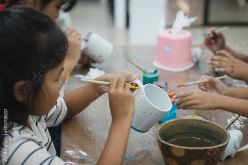 Asian child girl and friends are concentrating to paint on ceramic glass with oil color together with fun. Kids arts and crafts creative activity class in school.