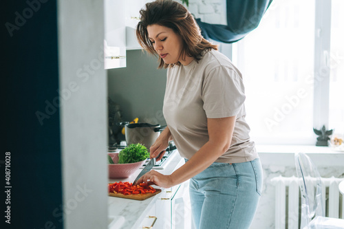 Beautiful brunette young woman plus size body positive cooking salad in kitchen at the home