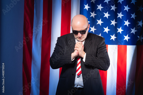 Man prays on background of American flag. He works as lobbyists America. Employee of a lobbying company USA. lobbying in United States of America. American lobbyist prays to god. Lobbying interests