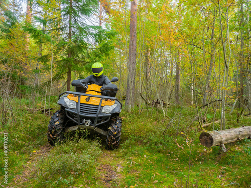 ATV rider during motocross. ATV rides through the forest. Man on a yellow quad cycle. ATV rider in taiga. He participates in an off-road race. Motocross in forest. Extreme sport on a bike