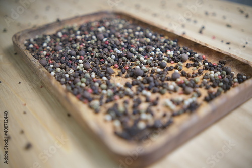 A mixture of Indian seasonings is poured into a wooden plate on a wooden table. Black pink pepper. Ingredients for the dish. selective focus.