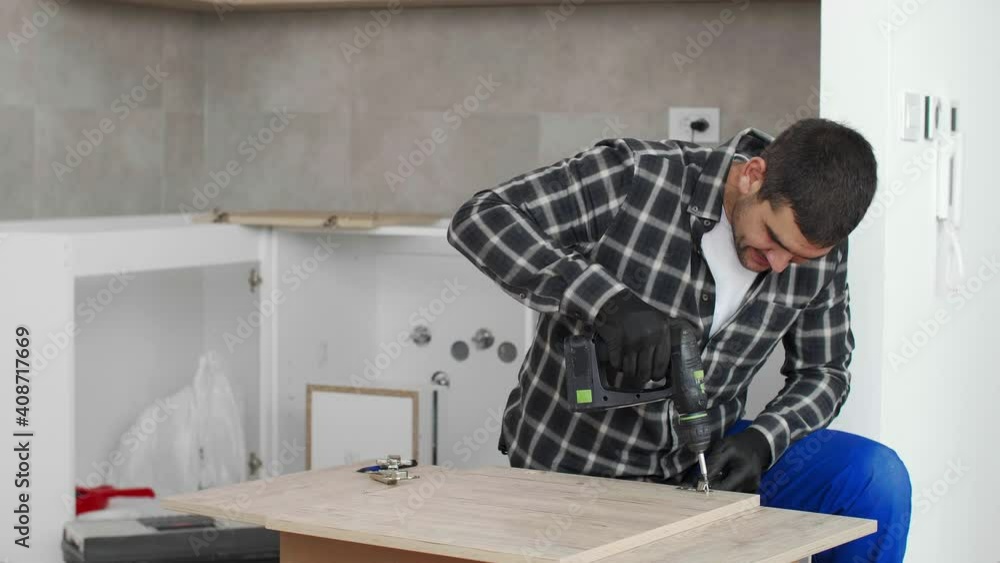 The carpenter screwing in and mounting hinge on kitchen shelves. The carpenter screwing in and mounting hinge on kitchen shelves.