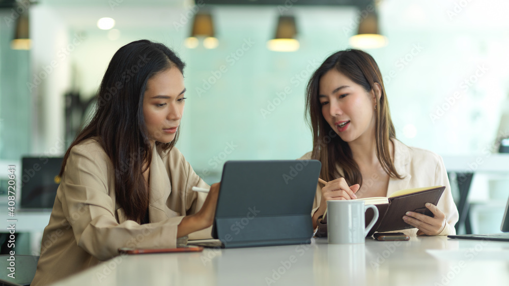 Two businesswomen talking to each other while working in meeting room Two businesswomen talking to each other while working in meeting room