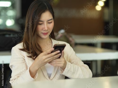 Female office worker using smartphone while relaxed sitting in cafeteria