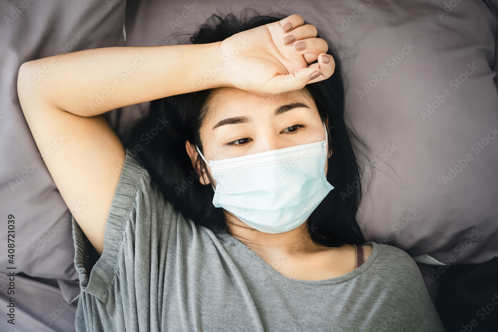 stressed Asian woman with protective face mask lying down in bed thinking or worry of sickness