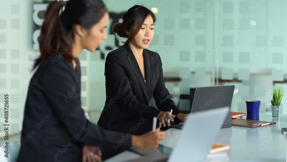 Two businesswomen working with laptops while sitting next to each other Two businesswomen working with laptops while sitting next to each other