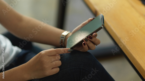 Female hands holding smartphone while sitting at workplace