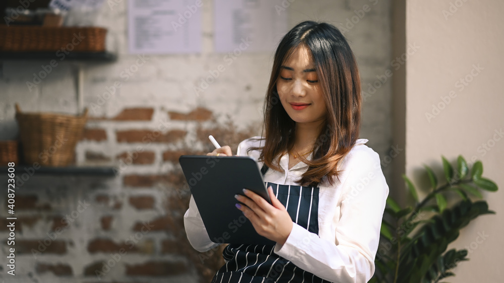 Smiling coffee shop owner standing inside her shop and using digital tablet receive orders from customers. Smiling coffee shop owner standing inside her shop and using digital tablet receive orders from customers.