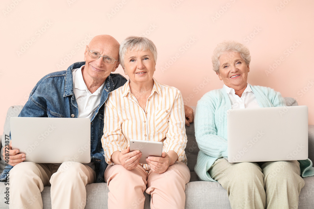 Senior people with different devices sitting on sofa in room Senior people with different devices sitting on sofa in room