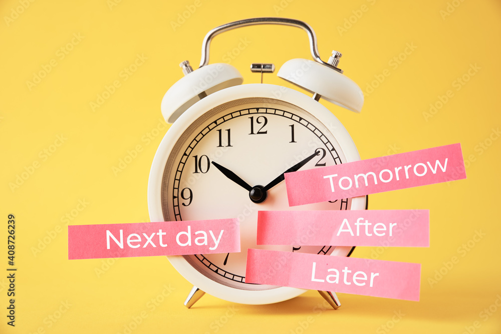 Procrastination, delay and postpone concept. Alarm clock with sticky notes later, tomorrow, next day and after on yellow background Procrastination, delay and postpone concept. Alarm clock with sticky notes later, tomorrow, next day and after on yellow background