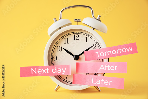 Procrastination, delay and postpone concept. Alarm clock with sticky notes   later, tomorrow, next day and after on yellow background