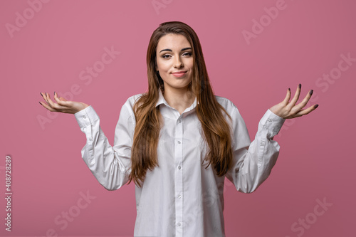Portrait of clueless and indecisive brunette girl shrugging with hands spread sideways, pink background