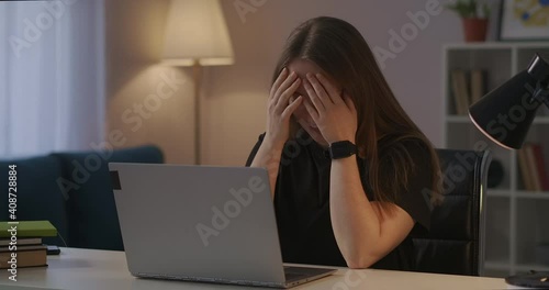 overworked woman is rubbing temples during working with laptop at home at evening, headache and overfatigue photo