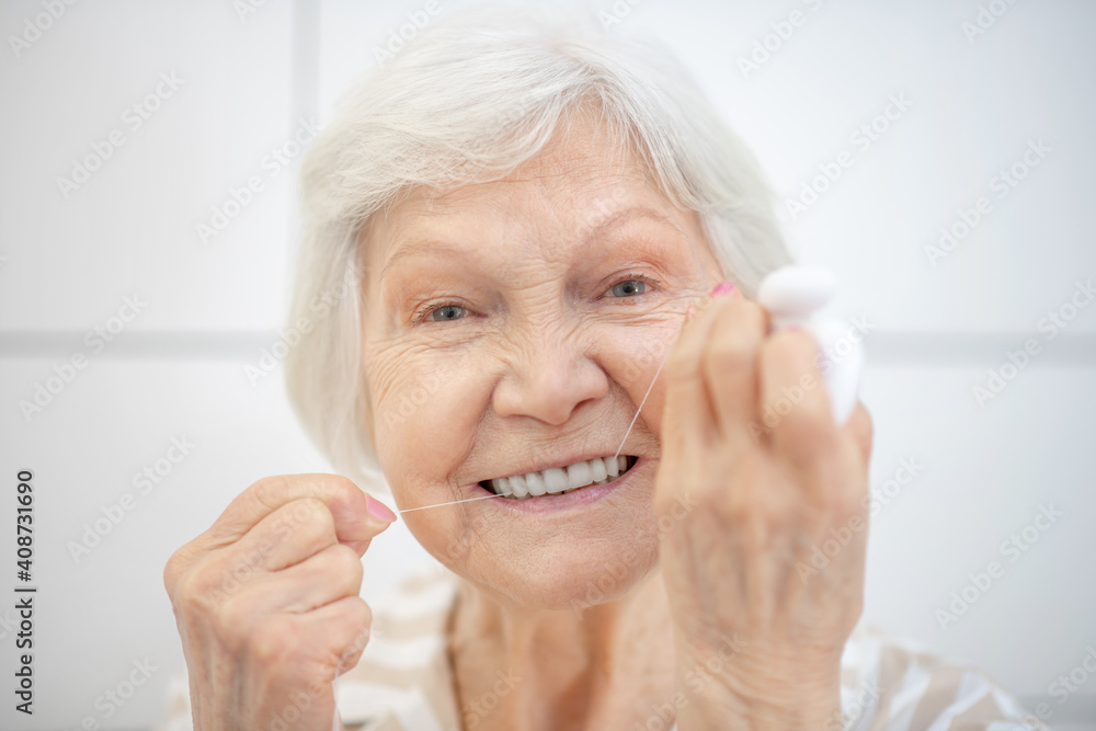 Gray-haired woman cleaning her teeth and using floss Gray-haired woman cleaning her teeth and using floss