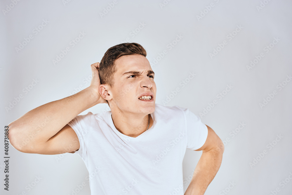 Emotional man in a white t-shirt holds his hand on his face light background Emotional man in a white t-shirt holds his hand on his face light background