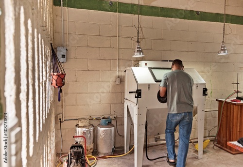 Ecuador, Galapagos Islands, Man sandblasting glass to make souvenir glasses out of bottles in artisan workshop