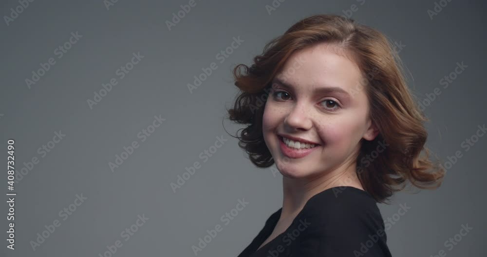 Happy young woman with medium long curly brown hair. Beautiful smiling girl posing at studio. Slow motion footage of an attractive brown-haired woman. Cheerful model turns to the camera. Happy young woman with medium long curly brown hair. Beautiful smiling girl posing at studio. Slow motion footage of an attractive brown-haired woman. Cheerful model turns to the camera.