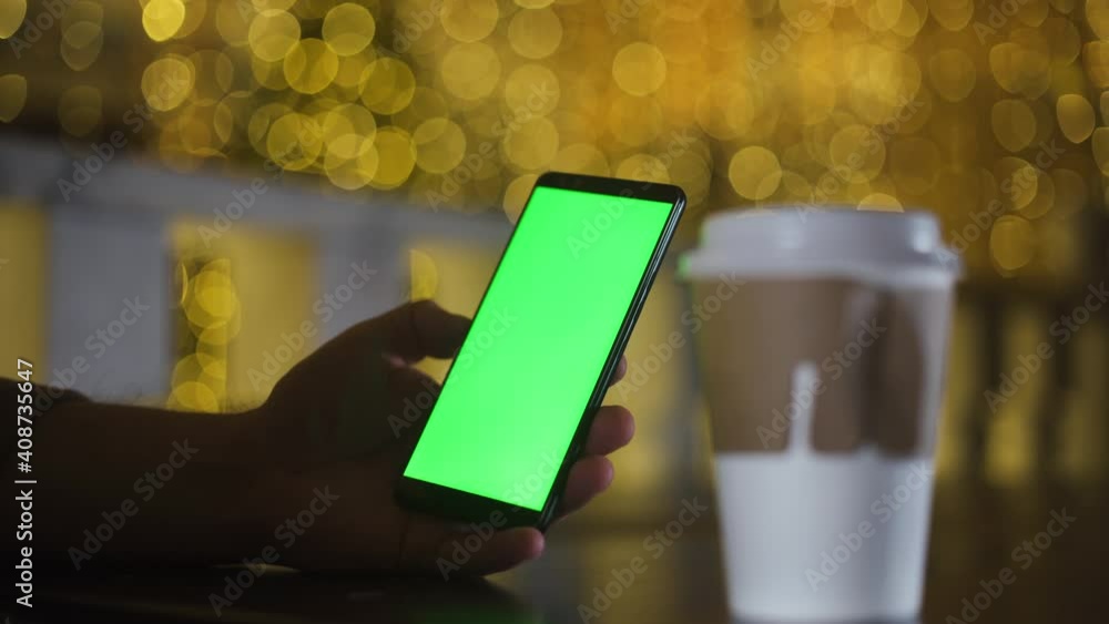 Close-up of a man's hand holding green screen smartphone mock-up. Near paper cup coffee to go. Man with telephone. Modern cell phone. Chroma key cellphone greenscreen new technology concept. Close-up of a man's hand holding green screen smartphone mock-up. Near paper cup coffee to go. Man with telephone. Modern cell phone. Chroma key cellphone greenscreen new technology concept.