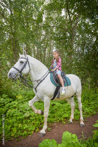 A teenage girl and a horse in nature among green trees © keleny