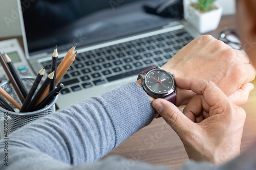 Close-up image of fashion luxury brown watch on wrist of man. Businessman working with laptop on desk office. Watching and checking the time on his wrist watch, a clock on his hands.