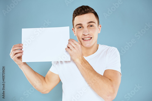 A man in a white t-shirt holds in his hands a sheet of paper emotions cropped view of a blue background Copy Space