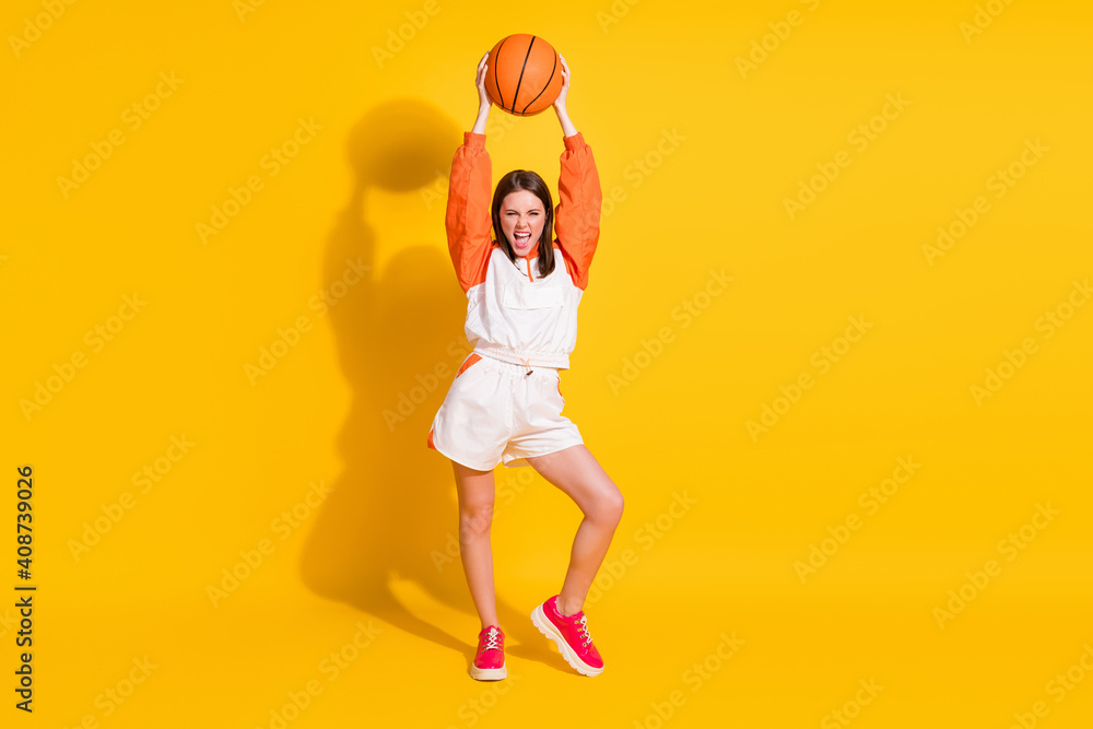 Full length photo portrait of celebrating woman holding basketball over head isolated on vivid yellow colored background