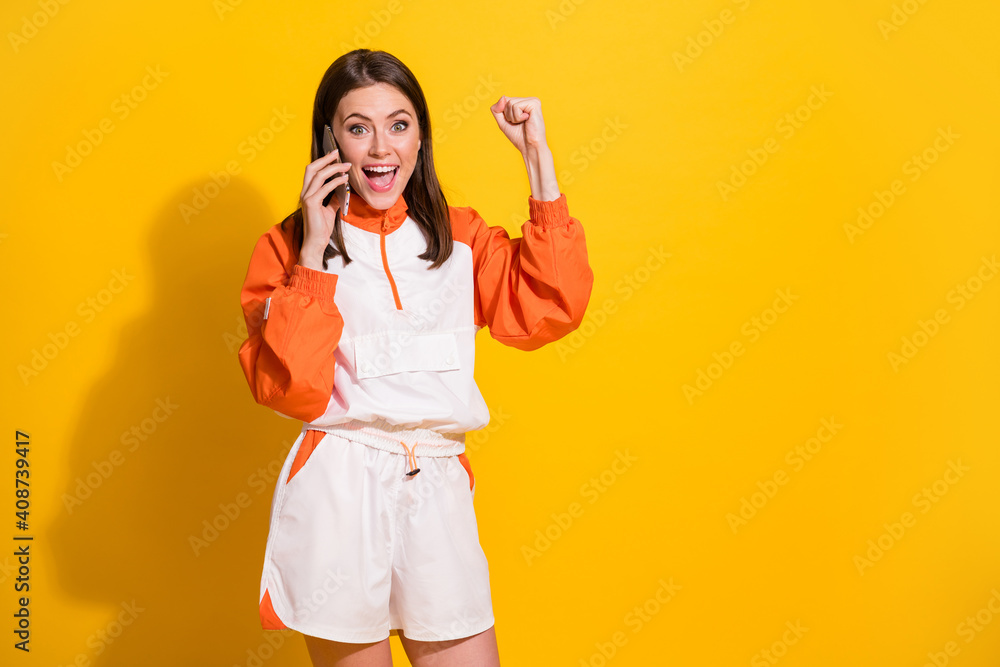 Photo portrait of celebrating girl with raised fist talking on phone isolated on vivid yellow colored background Photo portrait of celebrating girl with raised fist talking on phone isolated on vivid yellow colored background