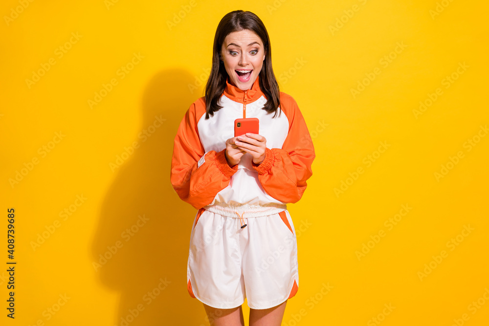 Photo portrait of excited woman with open mouth holding phone in two hands isolated on vivid yellow colored background Photo portrait of excited woman with open mouth holding phone in two hands isolated on vivid yellow colored background