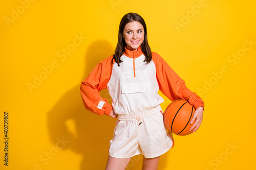 Photo portrait of dreamy woman holding basketball in one hand isolated on vivid yellow colored background