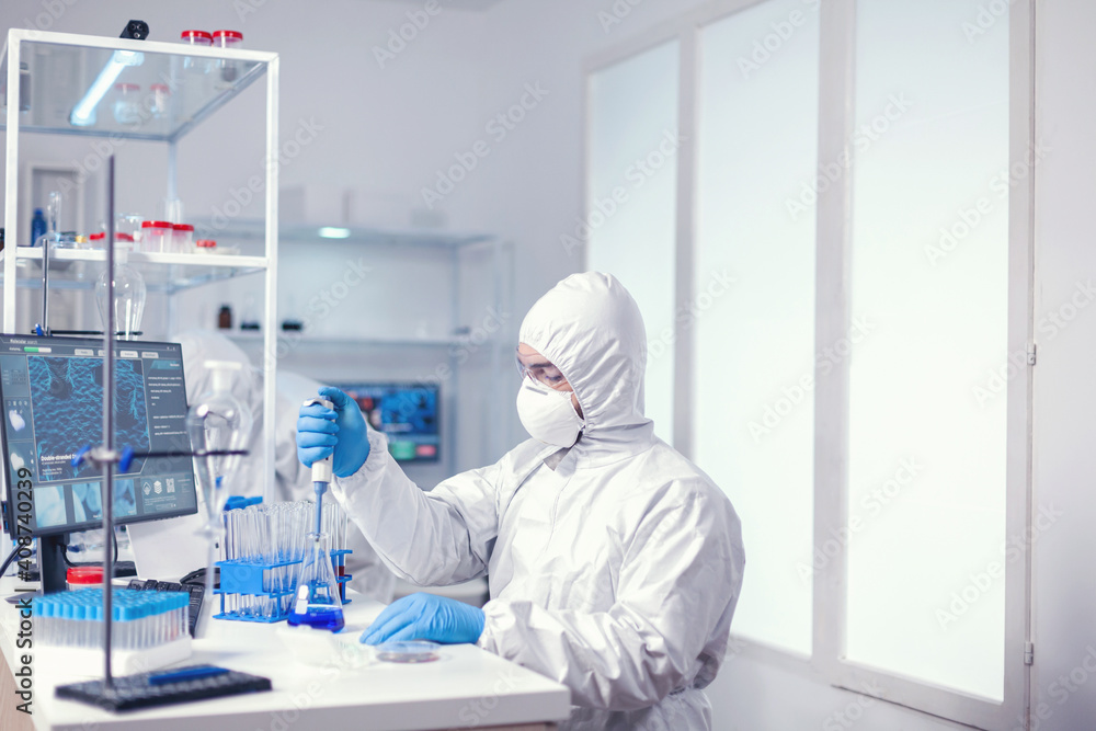 Naklejka premium Chemist in modern laboratory doing research using dispenser during global epidemic with covid-19.