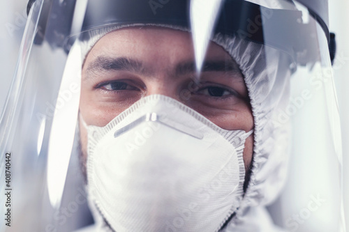 Medic with visor and ppe protection equipment looking at camera in laboratory. Overworked researcher dressed in protective suit against invection with coronavirus during global epidemic. photo