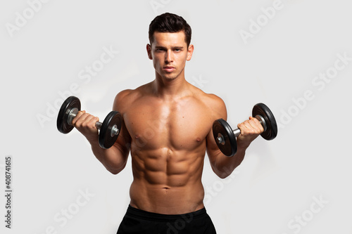 Front image of a confident young man with bare torso  training with dumb-bell  isolated white background. Horizontal view.