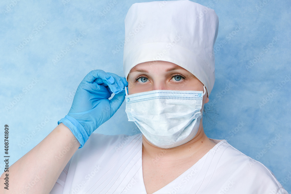 A nurse in a white coat, mask and gloves. On a blue background. Close-up. Place for an inscription. A nurse in a white coat, mask and gloves. On a blue background. Close-up. Place for an inscription.