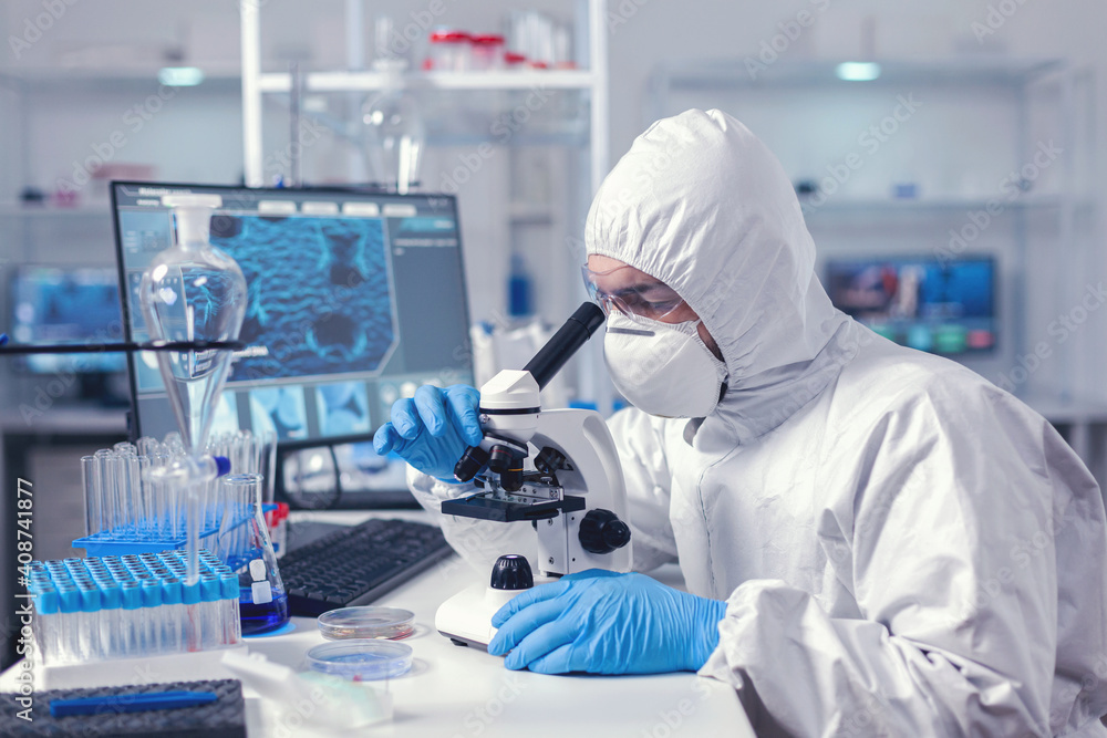 Scientist changing microscope lenses in time of coronavirus experiment dressed in ppe suit. Virolog in coverall during coronavirus outbreak conducting healthcare scientific analysis. Scientist changing microscope lenses in time of coronavirus experiment dressed in ppe suit. Virolog in coverall during coronavirus outbreak conducting healthcare scientific analysis.