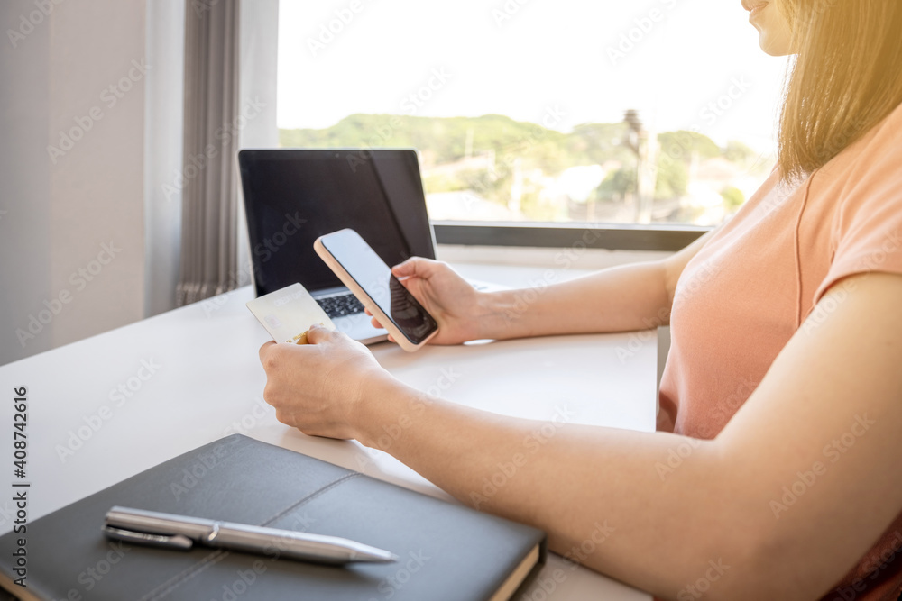 Young Asian consumer woman hand holding a credit card, Ready to spending pay online shopping according to discount products via smartphone and laptop from home Young Asian consumer woman hand holding a credit card, Ready to spending pay online shopping according to discount products via smartphone and laptop from home