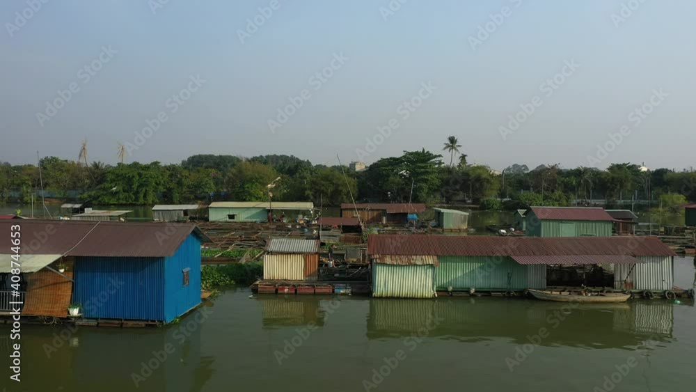 Floating fish farming community in Bien Hoa on the Dong Nai river, Vietnam on a sunny day. Drone tracking shot flying low above water.