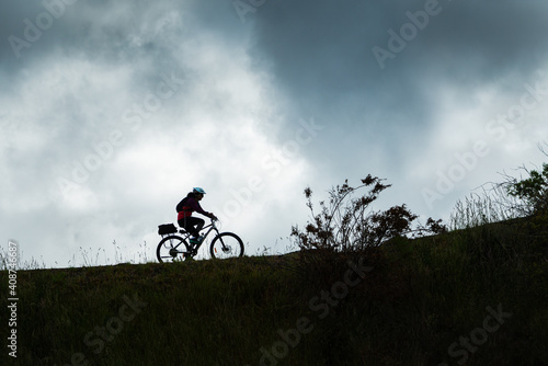 Silhouette image of a female cyclist riding the Otago Central Rail Trail against the cloudy sky, South Island, New Zealand