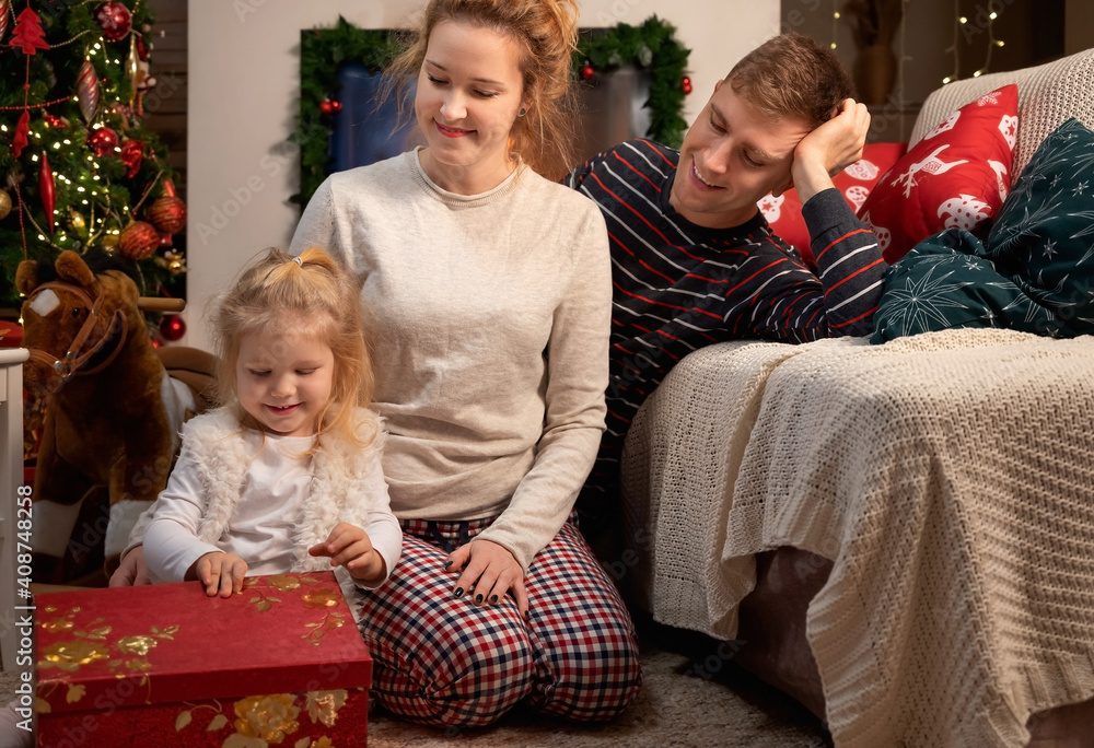 Little girl child with her young parents celebrating Christmas at home by the fireplace Little girl child with her young parents celebrating Christmas at home by the fireplace